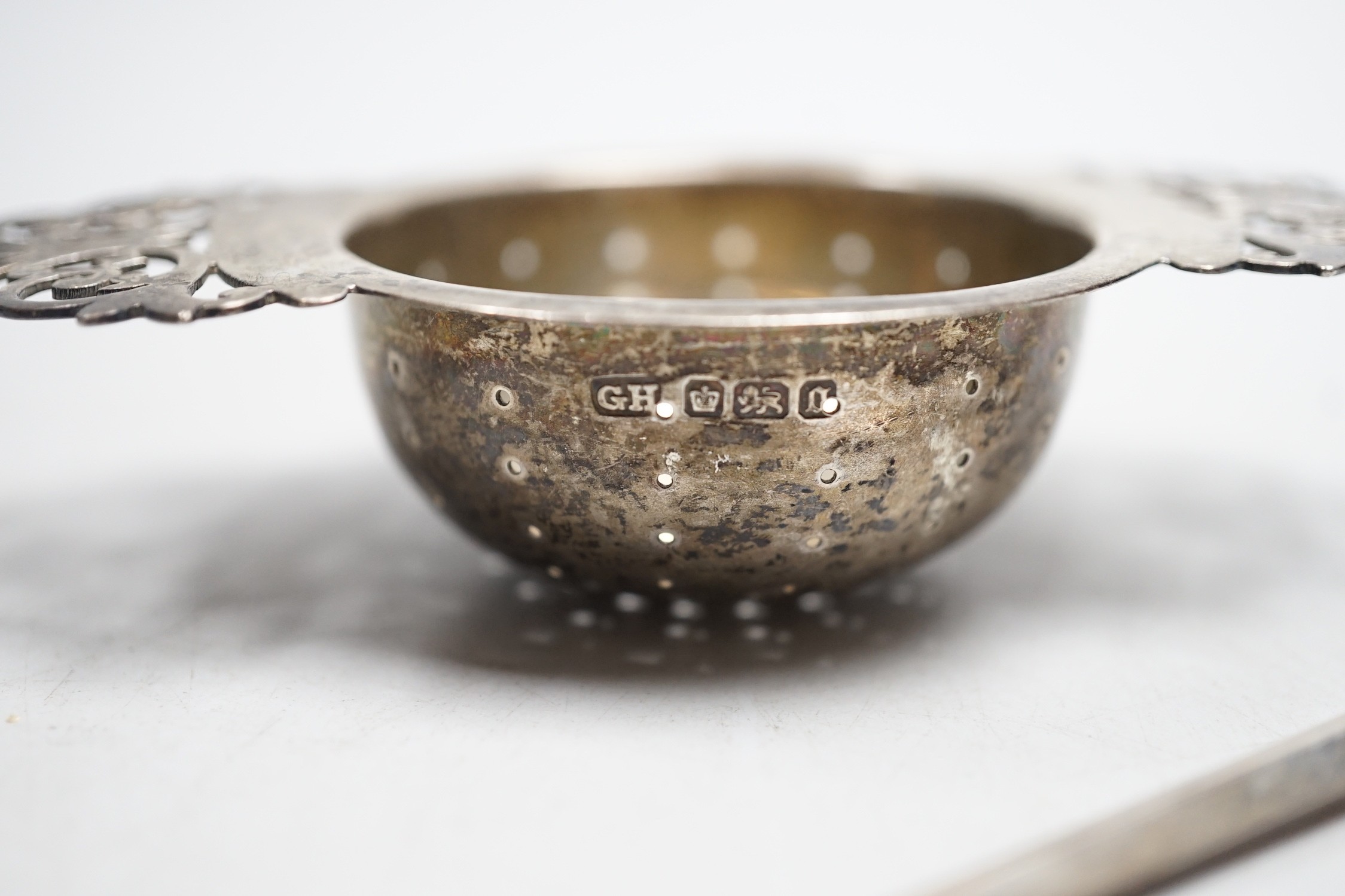 A silver tea strainer, a George III silver 'shovel' caddy spoon, London, 1811, a mother of pearl handled silver fruit knife and George IV silver game skewer, London, 1825, 14.7cm.